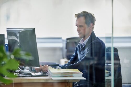 man working on computer in office behind glass